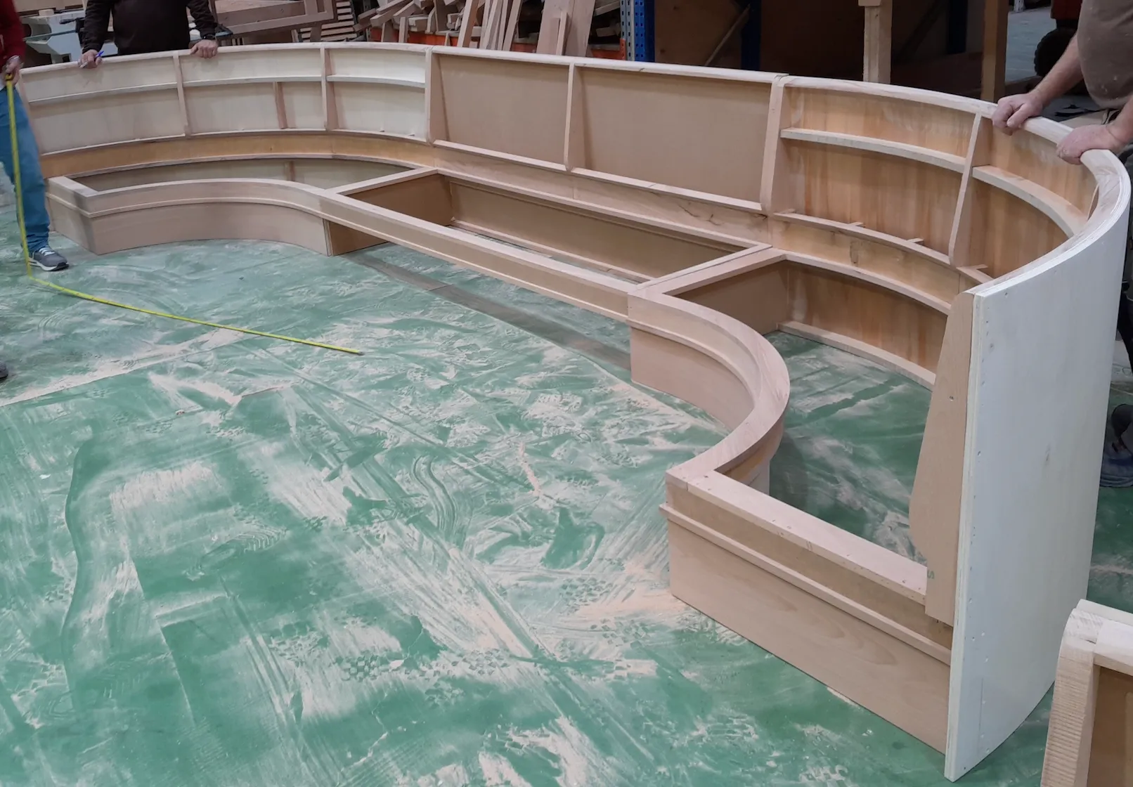 Curved timber banquette frame being measured in the workshop