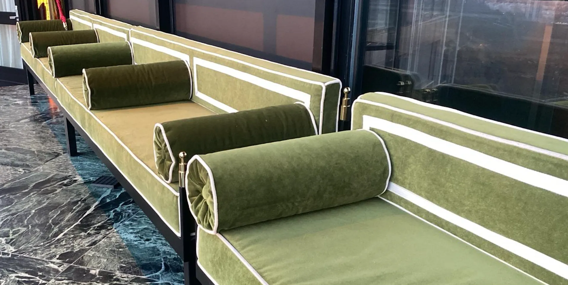 Green velvet banquettes with bolster cushions and brass details