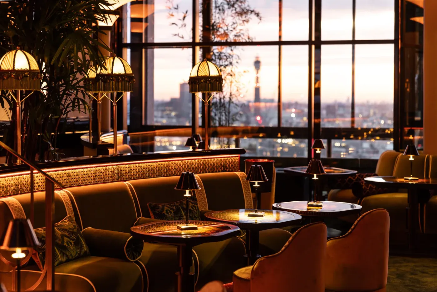 Lounge with velvet banquette seating, table lamps and city views at sunset