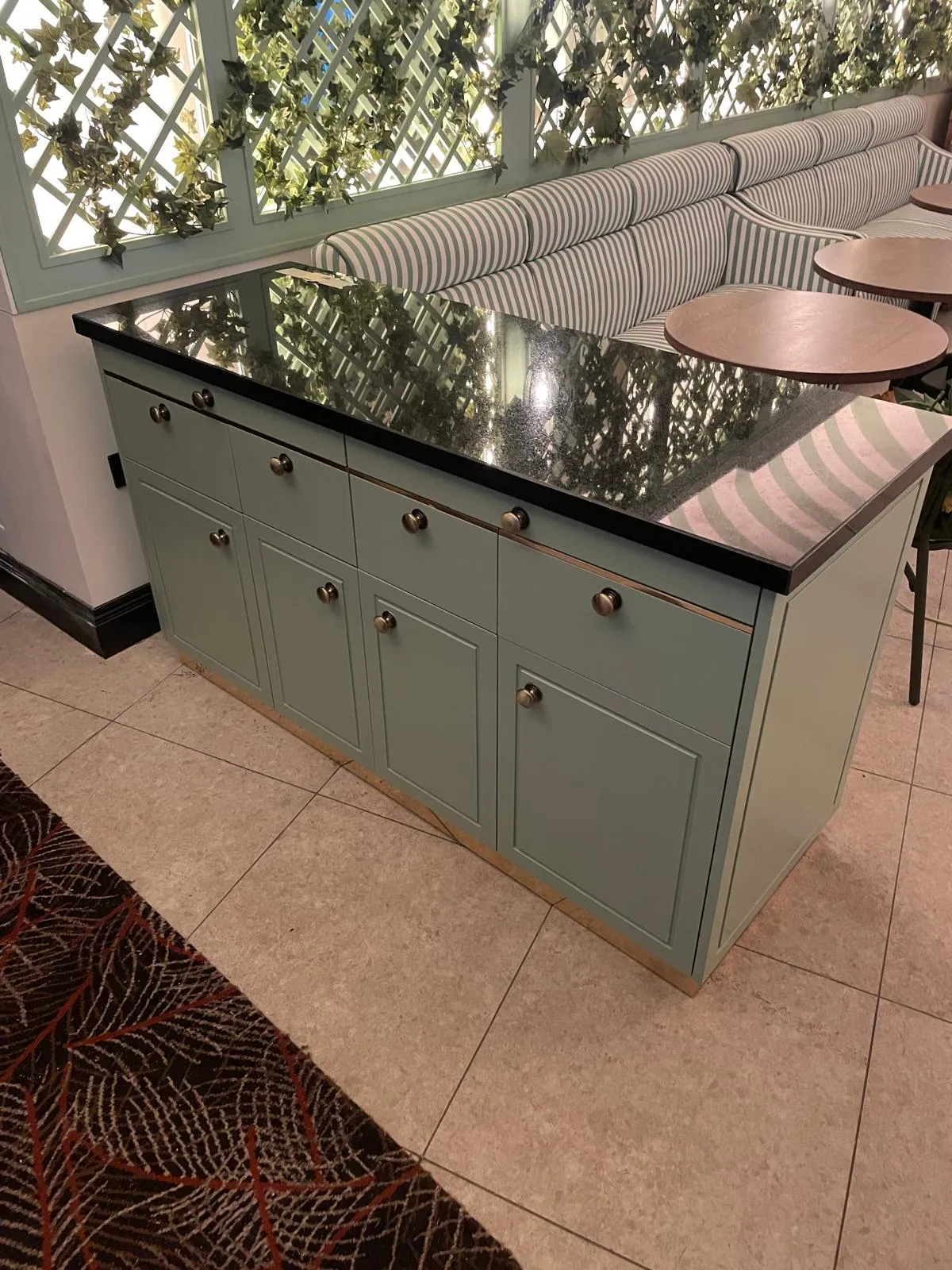 Sage green waiter station with a black stone top beside striped banquettes